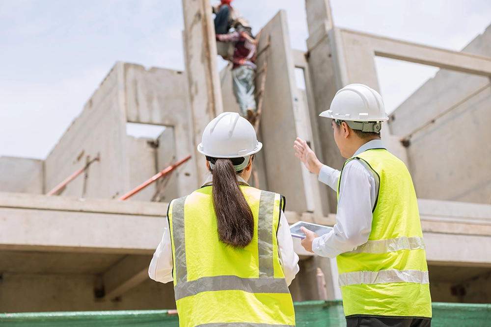 Sarı yelekli mühendis ve inşaat çalışanı, yüksek betonarme yapıya bakıyor